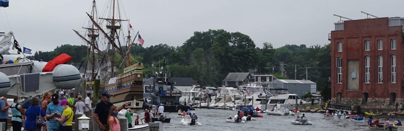 A busy harbor scene with a historic tall ship and numerous small boats on the water.