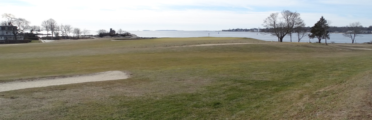 Expansive grassy landscape near a calm body of water under a clear sky.